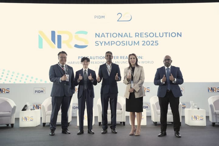 Five speakers standing together on stage at a symposium.